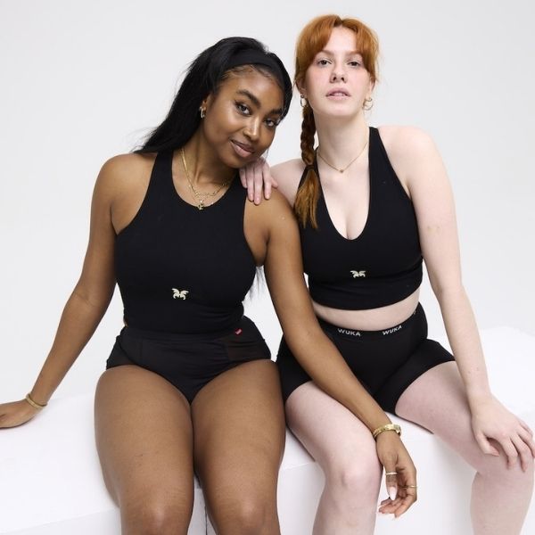 Two women sit confidently side by side wearing black WUKA period pants and crop tops, showcasing comfort, strength, and solidarity.