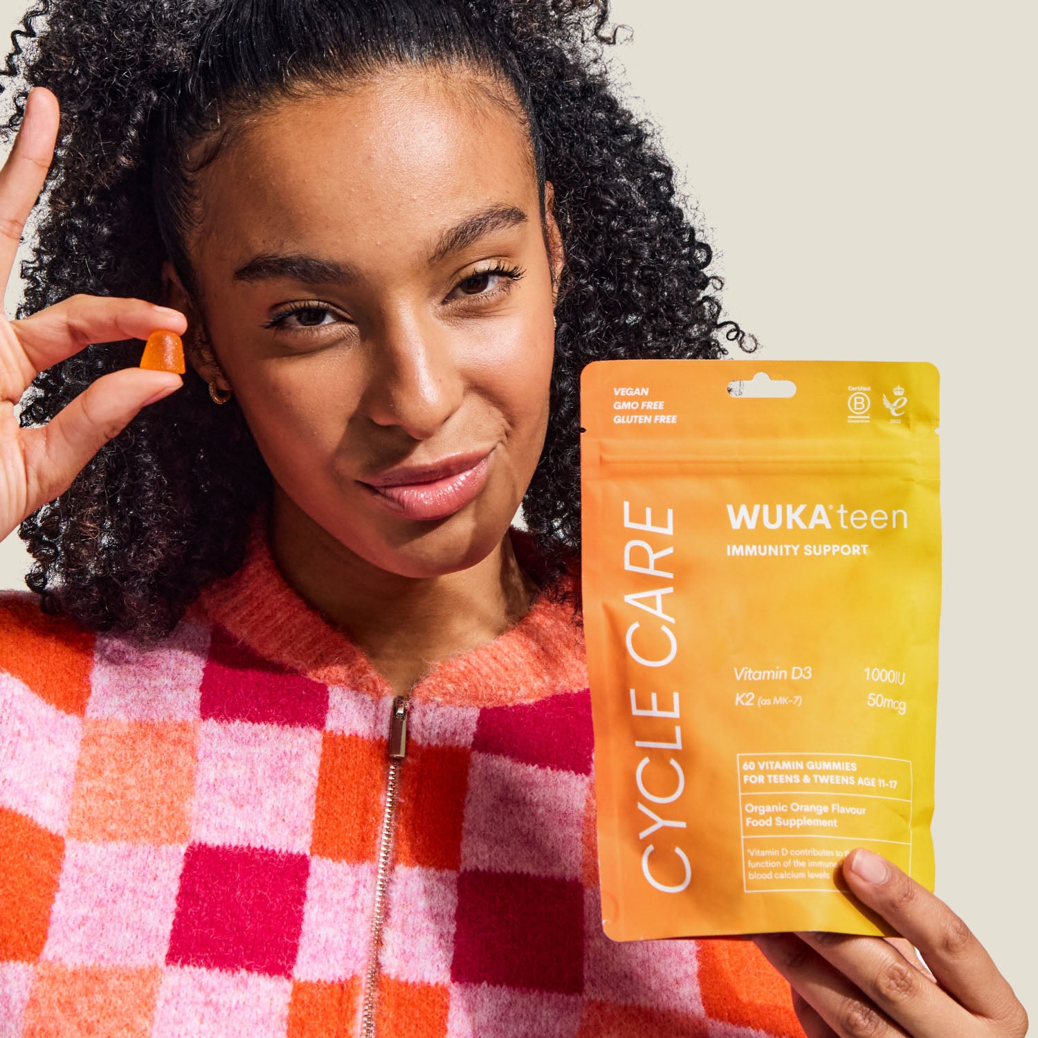 Smiling teenage girl holding WUKA teen immunity support gummies and an orange gummy, promoting daily immune support with vitamin D3 and K2.